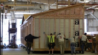 caption: Workers at Blazer Industries push a half-built portable classroom out the door of the modular building manufacturing plant in Aumsville, Oregon.
