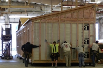 caption: Workers at Blazer Industries push a half-built portable classroom out the door of the modular building manufacturing plant in Aumsville, Oregon.