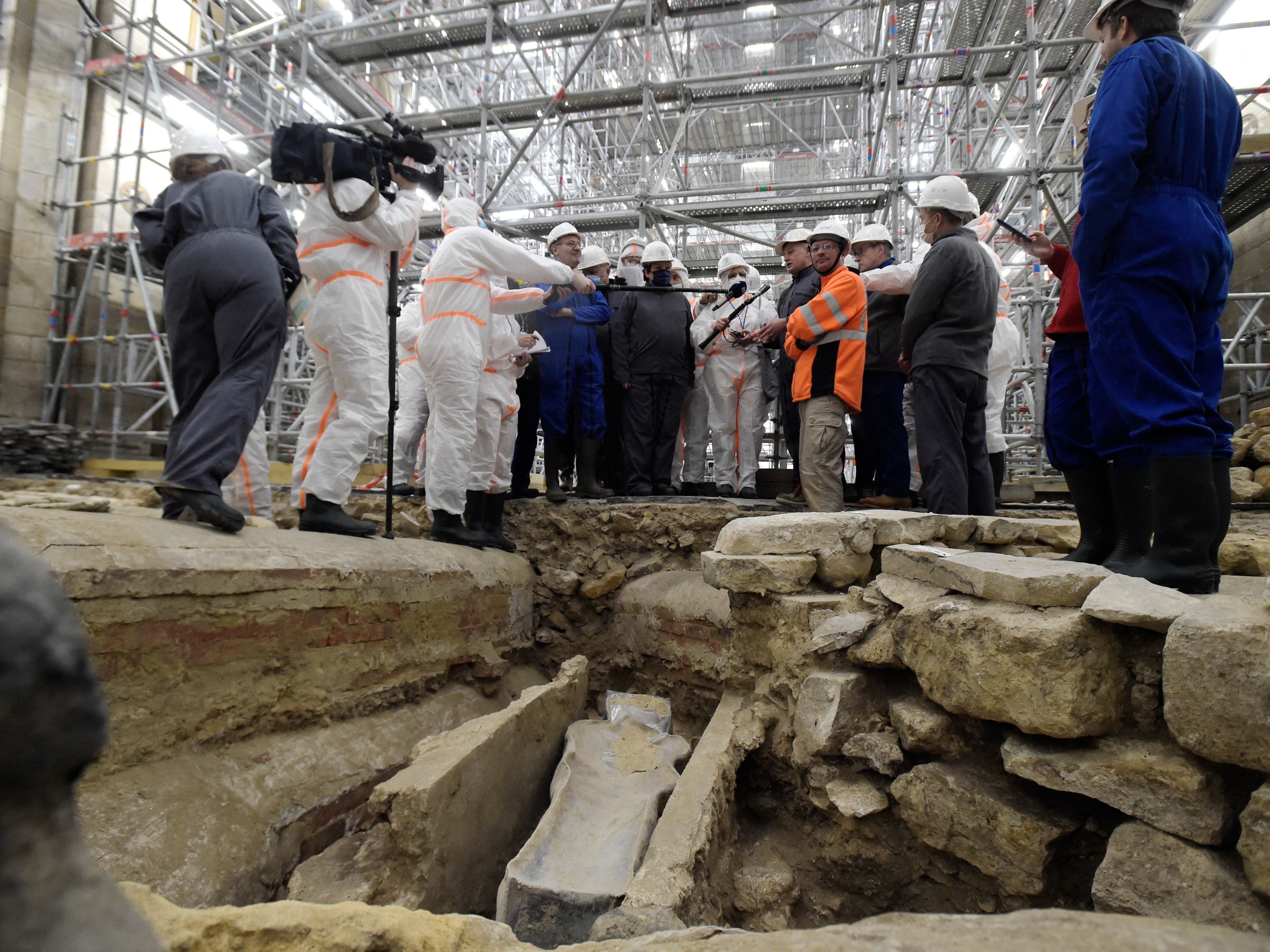 caption: France's Culture Minister Roselyne Bachelot (center left) visits the Notre Dame Cathedral archaeological research site in Paris on March 15 after the discovery of a 14th century lead sarcophagus.