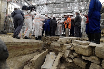 caption: France's Culture Minister Roselyne Bachelot (center left) visits the Notre Dame Cathedral archaeological research site in Paris on March 15 after the discovery of a 14th century lead sarcophagus.
