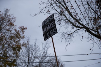 caption: A sign that reads 'house the homeless' is shown on Wednesday, December 16, 2020, near an encampment of unhoused community members at Cal Anderson Park in Seattle. 