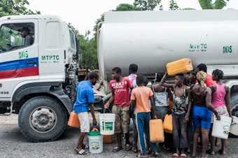 caption: People gather near bins of water in Camp-Perrin, Haiti, on Monday.