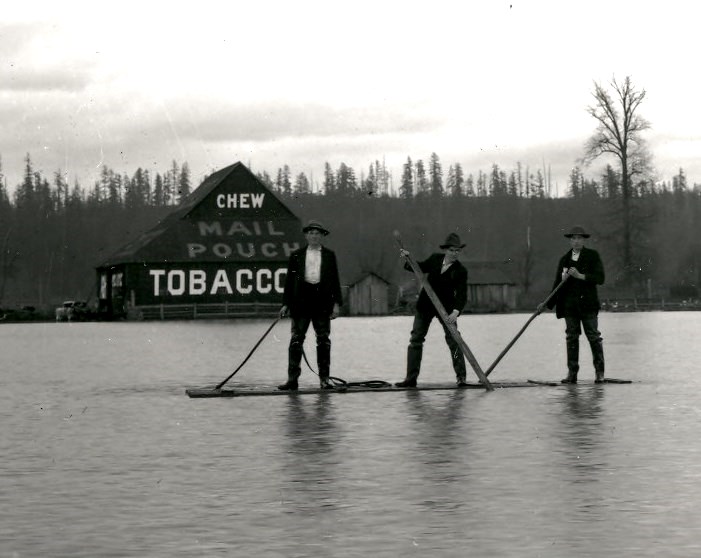 caption: A couple Kent farmers known as the Johnson brothers and an unidentified hired man stare down the photographer from a raft during a 1910 flood in what we today call The Green River Valley.