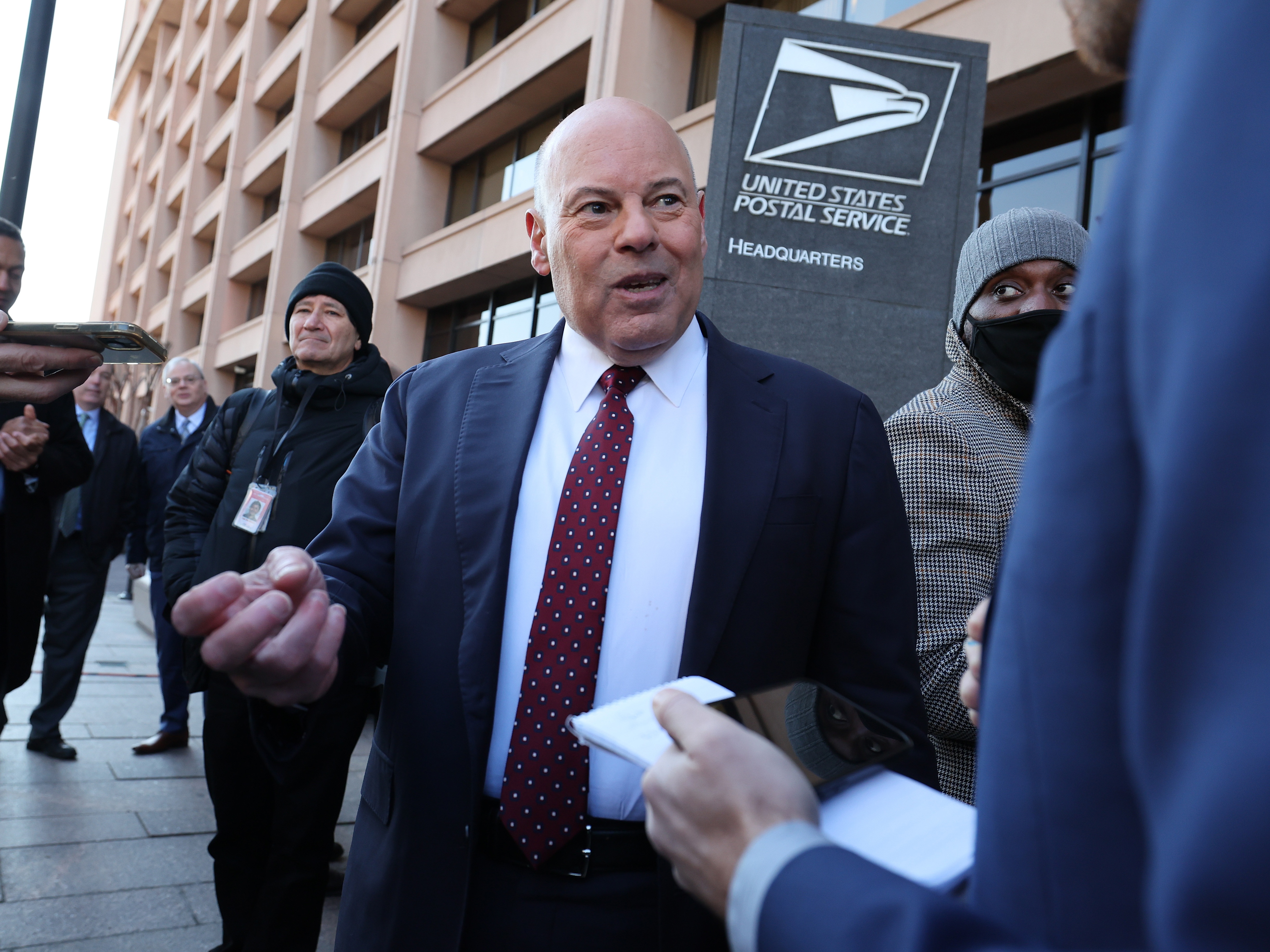 caption: Louis DeJoy, the outgoing U.S. postmaster general, speaks to reporters in 2022 in Washington, D.C. On Monday, he announced that he is stepping down.