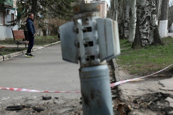 caption: A man walks past an unexploded tail section of a 300mm rocket which appear to contained cluster bombs launched from a BM-30 Smerch multiple rocket launcher embedded in the ground after shelling in Lysychansk, Lugansk region on April 11, 2022.