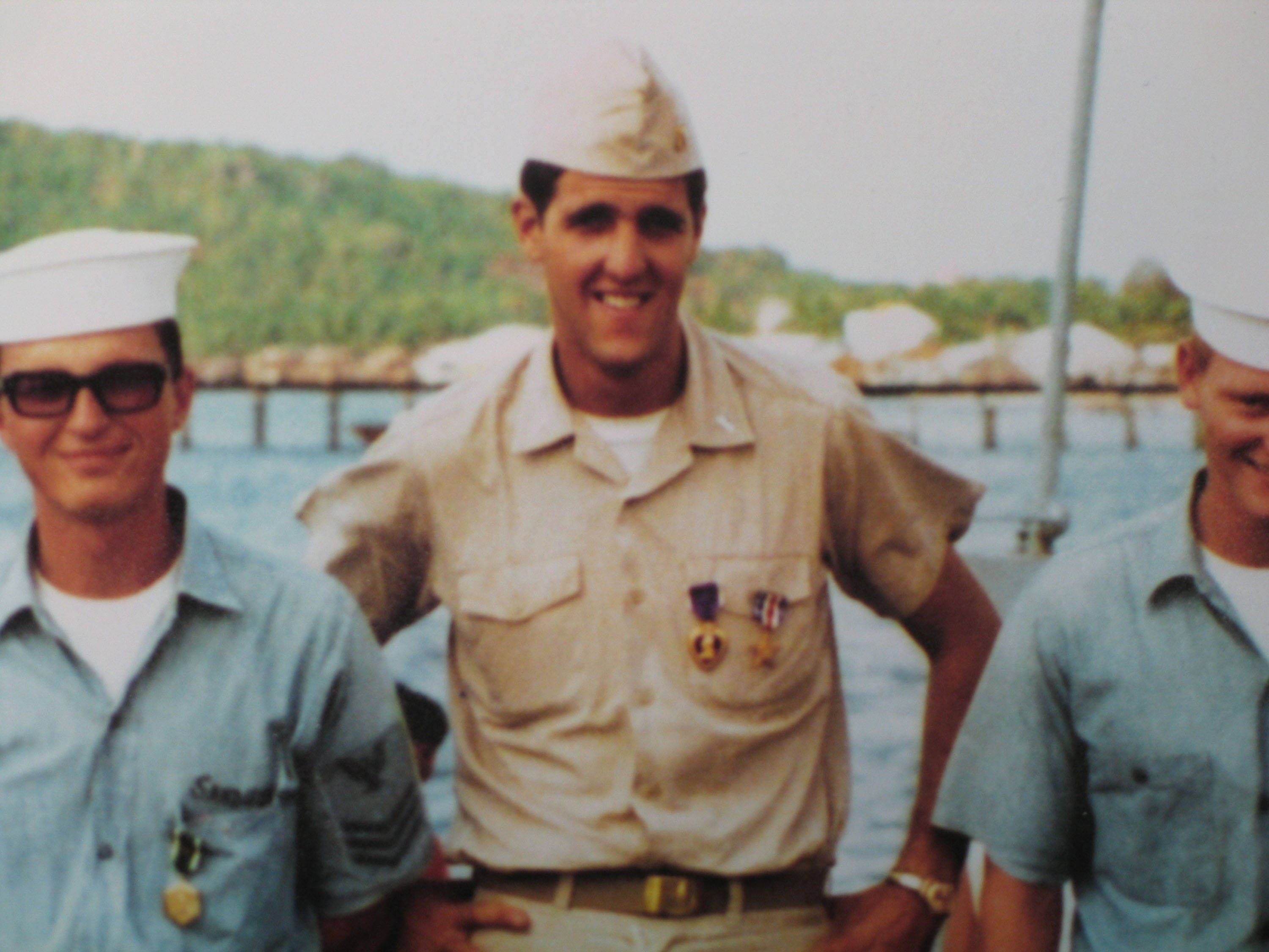 caption: John Kerry (center) stands with other military personnel in an unspecified location circa the 1960s. The details of Kerry's service during the Vietnam War, and his subsequent anti-war activism, became the focus of a veterans' group's smear campaign against him during his 2004 presidential campaign.