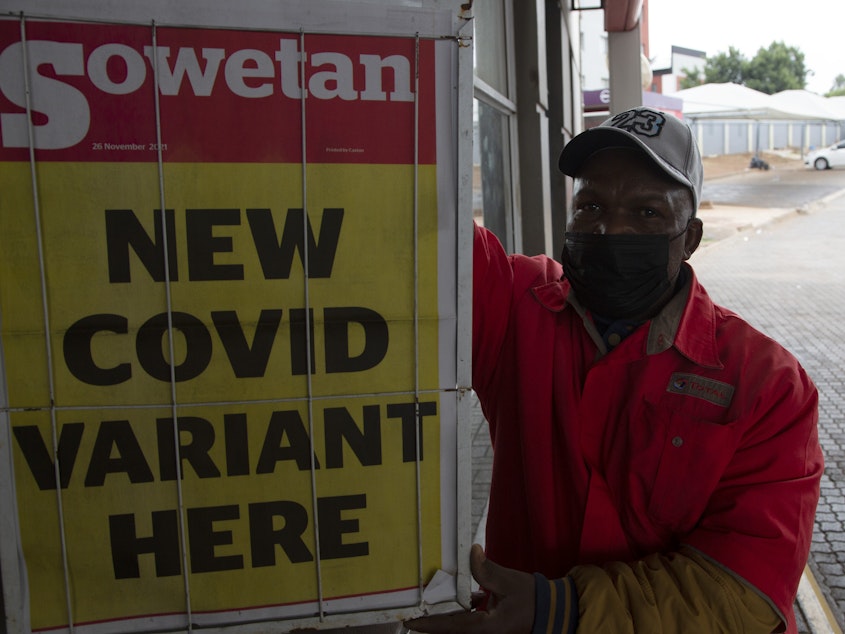 caption: A gas station attendant stands next to a newspaper headline in Pretoria, South Africa, on Saturday. The new omicron variant has spread from South Africa to parts of Europe, and as far as Hong Kong.