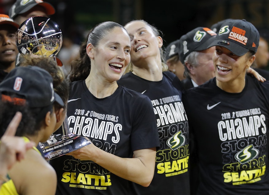 caption: Seattle Storm guard Sue Bird, left, holds the championship trophy with her teammates Sami Whitcomb (center) and Alysha Clark (right) after winning Game 3 of the WNBA basketball finals, Wednesday, Sept. 18 2018, in Fairfax, Va. The Storm won 98-82. 