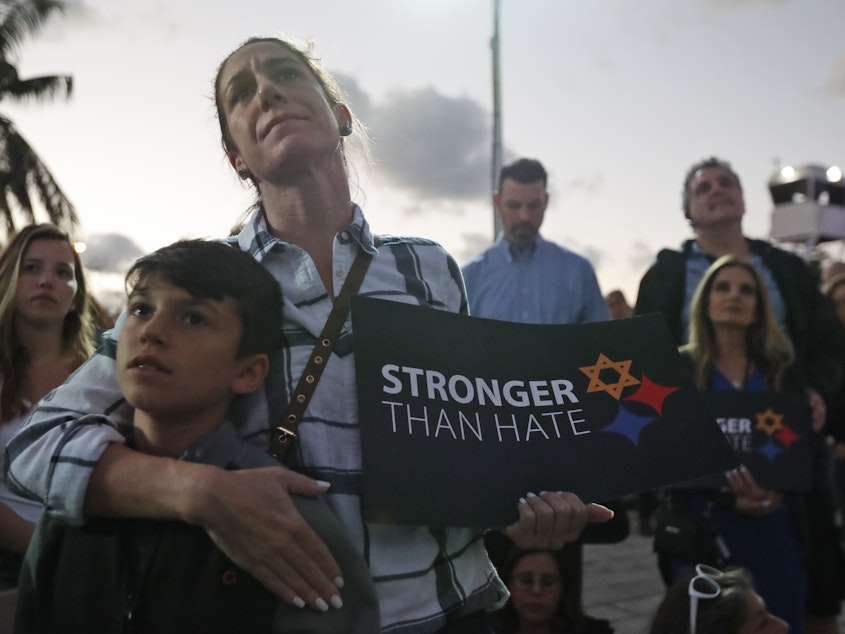 caption: Taly Kogon and her son Leo, 10, listen to speakers during an interfaith vigil against anti-semitism and hate at the Holocaust Memorial in Miami Beach, Fla.