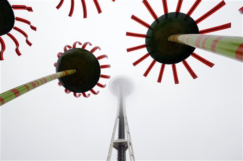 caption: Metal-sculpted flowers up to 40-feet tall frame the 605-foot Space Needle as it become obscured by fog on Wednesday.