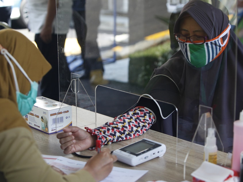 caption: Health workers measure a woman's blood pressure during a simulation of a COVID-19 vaccine trial in Indonesia.