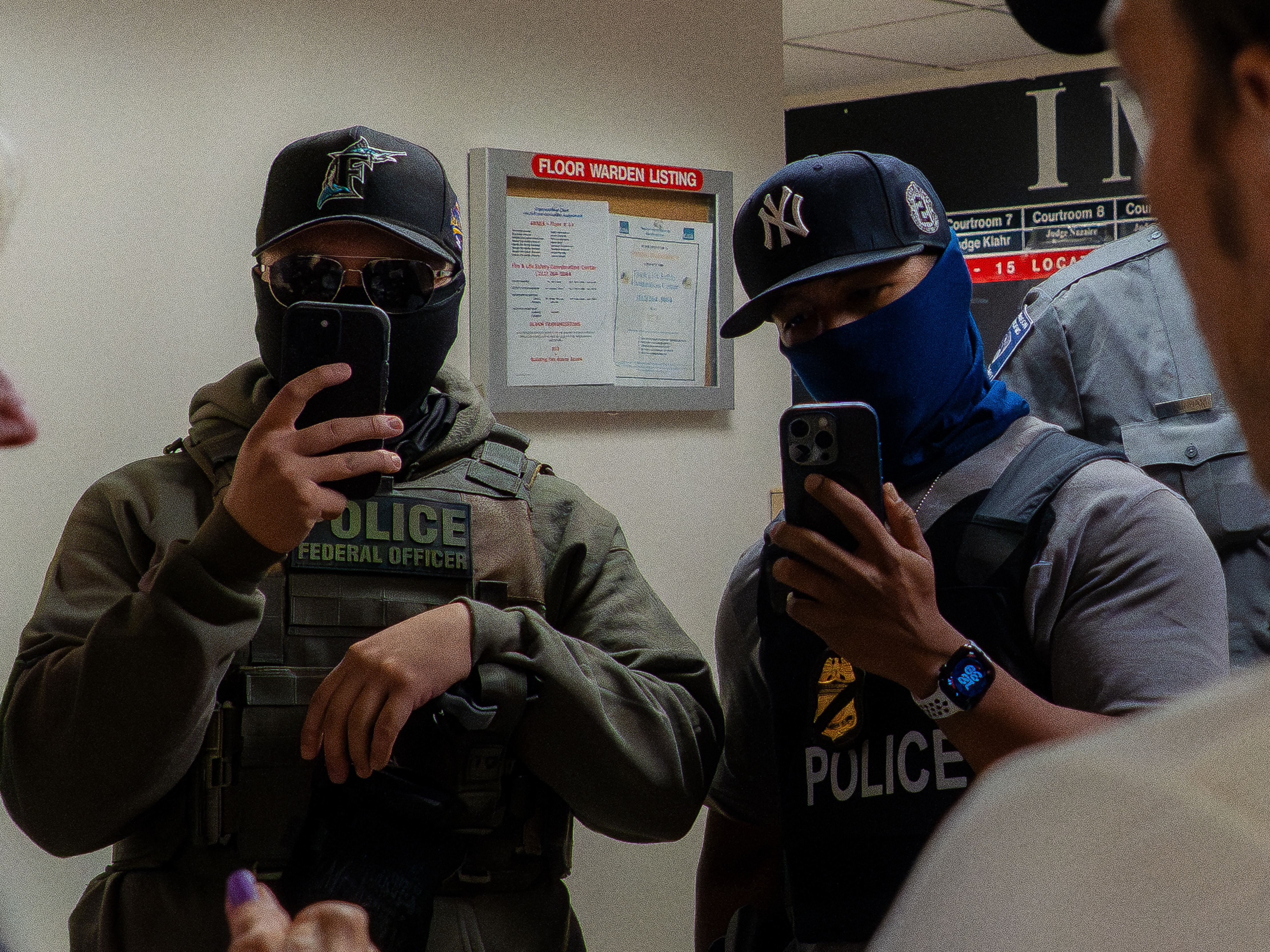 caption: Two ICE agents film the press using smartphones in the hallway outside the immigration court at 26 Federal Plaza in New York USA on July 11 2025. The Department of Homeland Security has been acquiring new tools to identify people and monitor them.