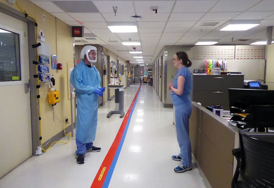 caption: Providers talk in the Covid ICU at the University of Washington Medical Center in Seattle on April 24, 2020. The red tape down the hallway indicates where medical staff may not go without personal protective gear. 