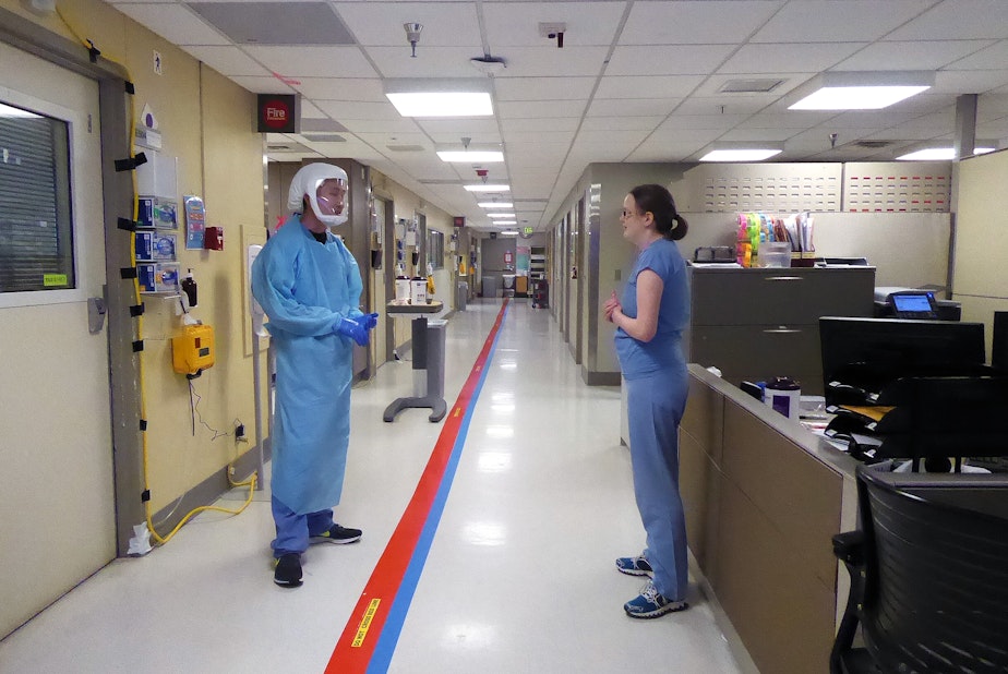 caption: Providers talk in the Covid ICU at the University of Washington Medical Center in Seattle on April 24, 2020. The red tape down the hallway indicates where medical staff may not go without personal protective gear. 