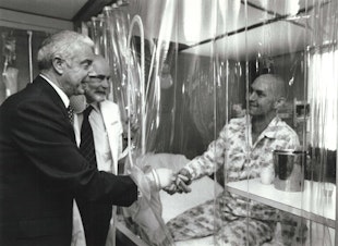 caption: Joe DiMaggio, Dr. E. Donnall Thomas, and patient Darrell Johnson in LAF (laminar airflow) room, 1978