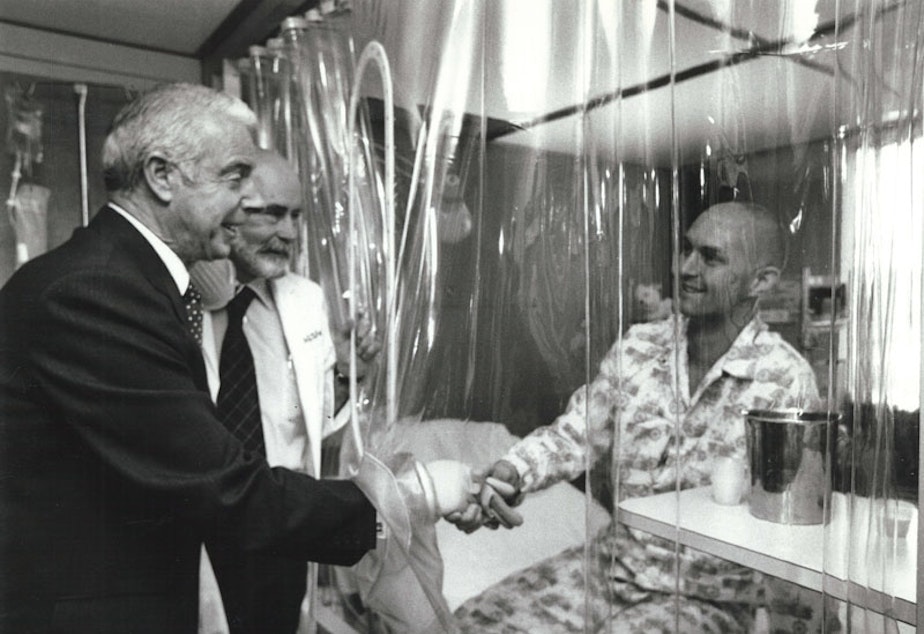 caption: Joe DiMaggio, Dr. E. Donnall Thomas, and patient Darrell Johnson in LAF (laminar airflow) room, 1978