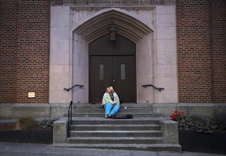 caption: Milee Ballweg, 20, sits on the steps of a church in the University District where she sleeps just after 5:00 a.m. on Wednesday, July 11, 2018, in Seattle.