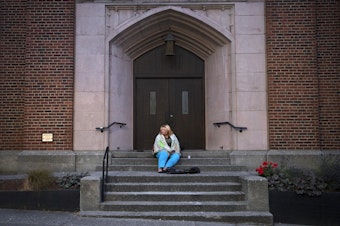 caption: Milee Ballweg, 20, sits on the steps of a church in the University District where she sleeps just after 5:00 a.m. on Wednesday, July 11, 2018, in Seattle.