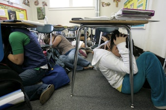 caption: Ninth-grade students, including Mahlia Butler, 15, right, take part in a statewide earthquake drill, Tuesday, April 24, 2007, as they "drop, cover, and hold" under their desks at King's High School, a private school near Seattle in Shoreline, Washington.