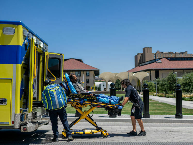 caption: EMTs help a patient in Austin, Texas, this week. The man had passed out near the state capitol and was dehydrated. Cities with few trees and areas of shade are hotter during heat waves.