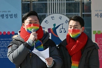 caption: So Seong-uk, left, speaks at a press conference while his partner Kim Yong-min looks on in February 2021 as they file a lawsuit against South Korea's National Health Insurance Service at the Seoul Administrative Court.