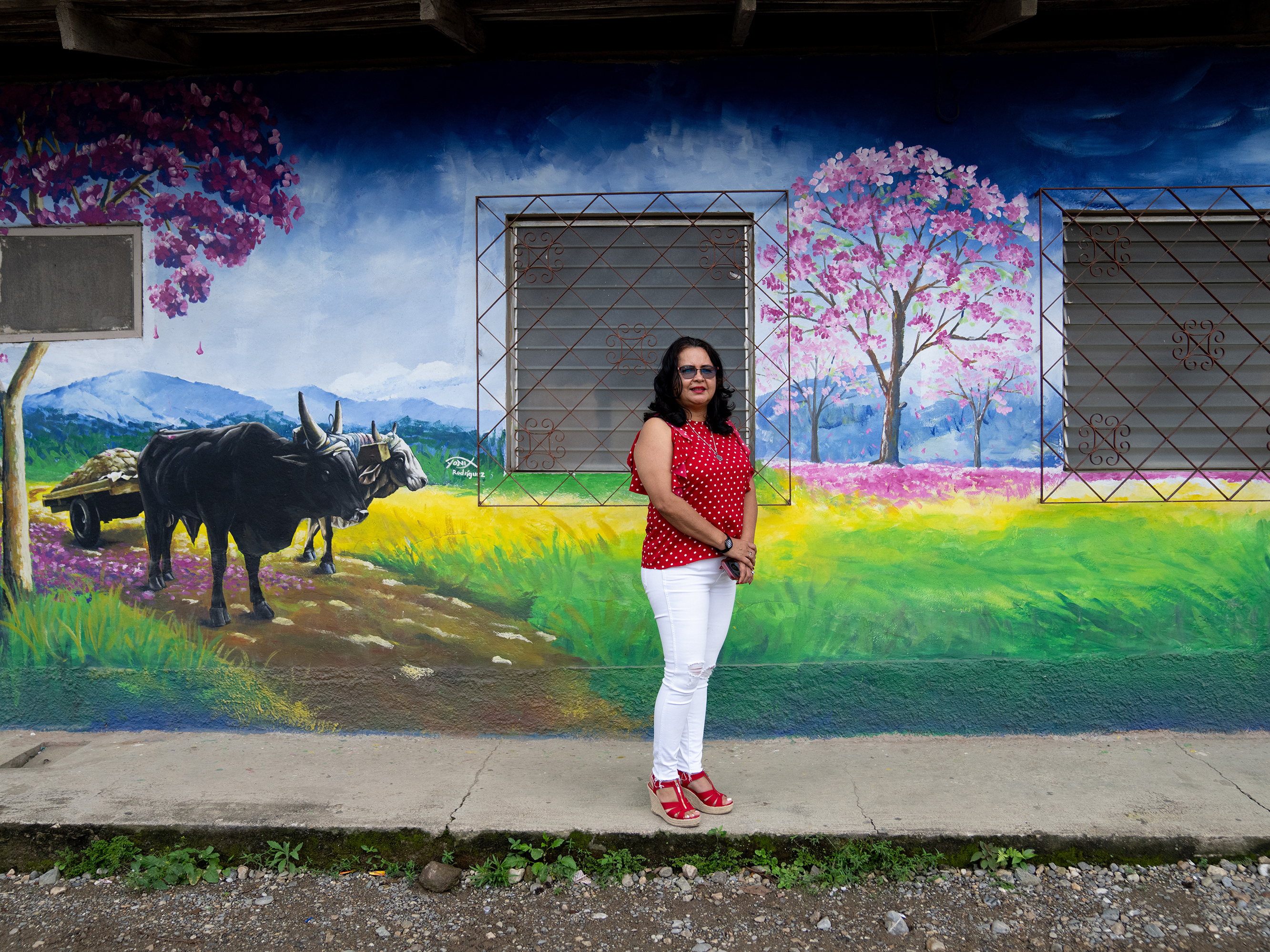 caption: Jacqueline Trejo, mayor of Macuelizo, walks past one of the town's murals. The pink flowering tree that's depicted is the source of the town's name. She wanted to improve the quality of life there but lacked the funds to fulfill her plans.