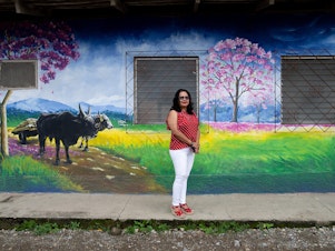 caption: Jacqueline Trejo, mayor of Macuelizo, walks past one of the town's murals. The pink flowering tree that's depicted is the source of the town's name. She wanted to improve the quality of life there but lacked the funds to fulfill her plans.