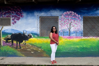 caption: Jacqueline Trejo, mayor of Macuelizo, walks past one of the town's murals. The pink flowering tree that's depicted is the source of the town's name. She wanted to improve the quality of life there but lacked the funds to fulfill her plans.