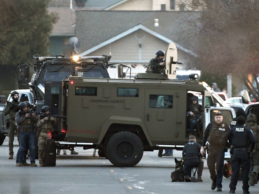 caption: Law enforcement officers aim their weapons at a home during a standoff in Grants Pass, Ore., on Tuesday, Jan. 31, 2023. Police said the standoff involving a man suspected in a violent kidnapping in Oregon who was barricaded underneath the home had been "resolved."