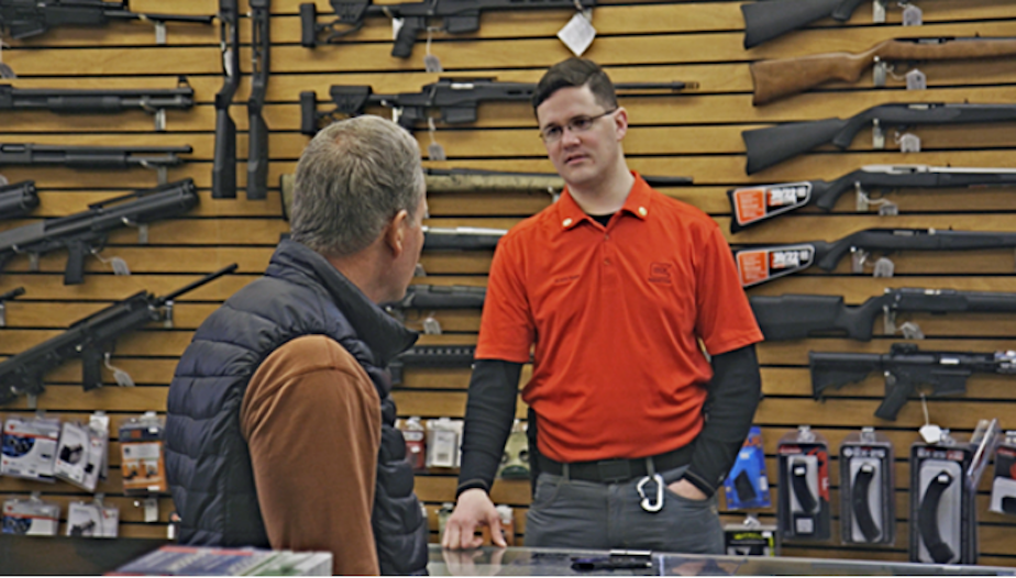 caption: Brett Bass, a gun retailer and coordinator of Forefront Suicide Prevention's Safer Homes, Suicide Aware program, talks with a customer about firearm safety.