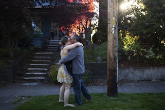 caption: Bethany Morrow, left, shares a kiss with partner Jeremy Lightsmith, right, after dancing along to the music as the Seattle Quarantine Parade drove through their neighborhood on Friday, May 8, 2020, in Seattle. 