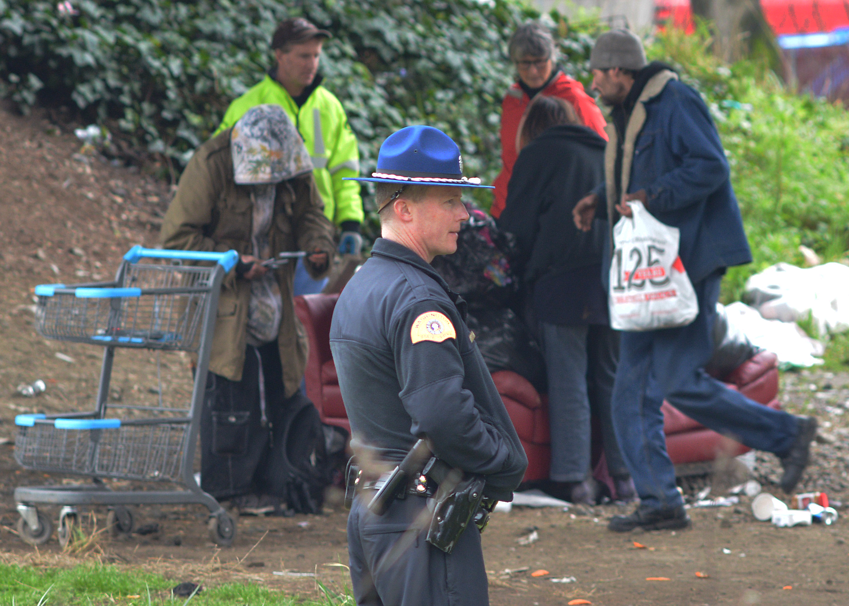 caption: A Washington State Patrol trooper looks on as a homeless camp is cleaned out at the corner of Airport Way South and South Royal Brougham Way on Wednesday, January 27, 2016. That's a short way from where two people were shot to death in 'The Jungle.'