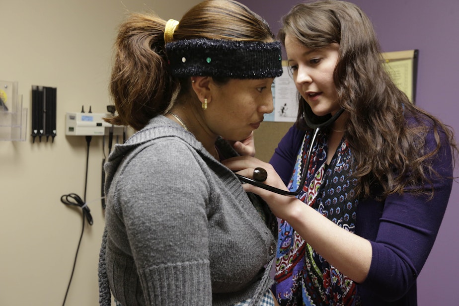caption: FILE: In this March 28, 2013 photo, medical resident Stephanie Place examines Maria Cazho at the Erie Family Health Center, in Chicago. 