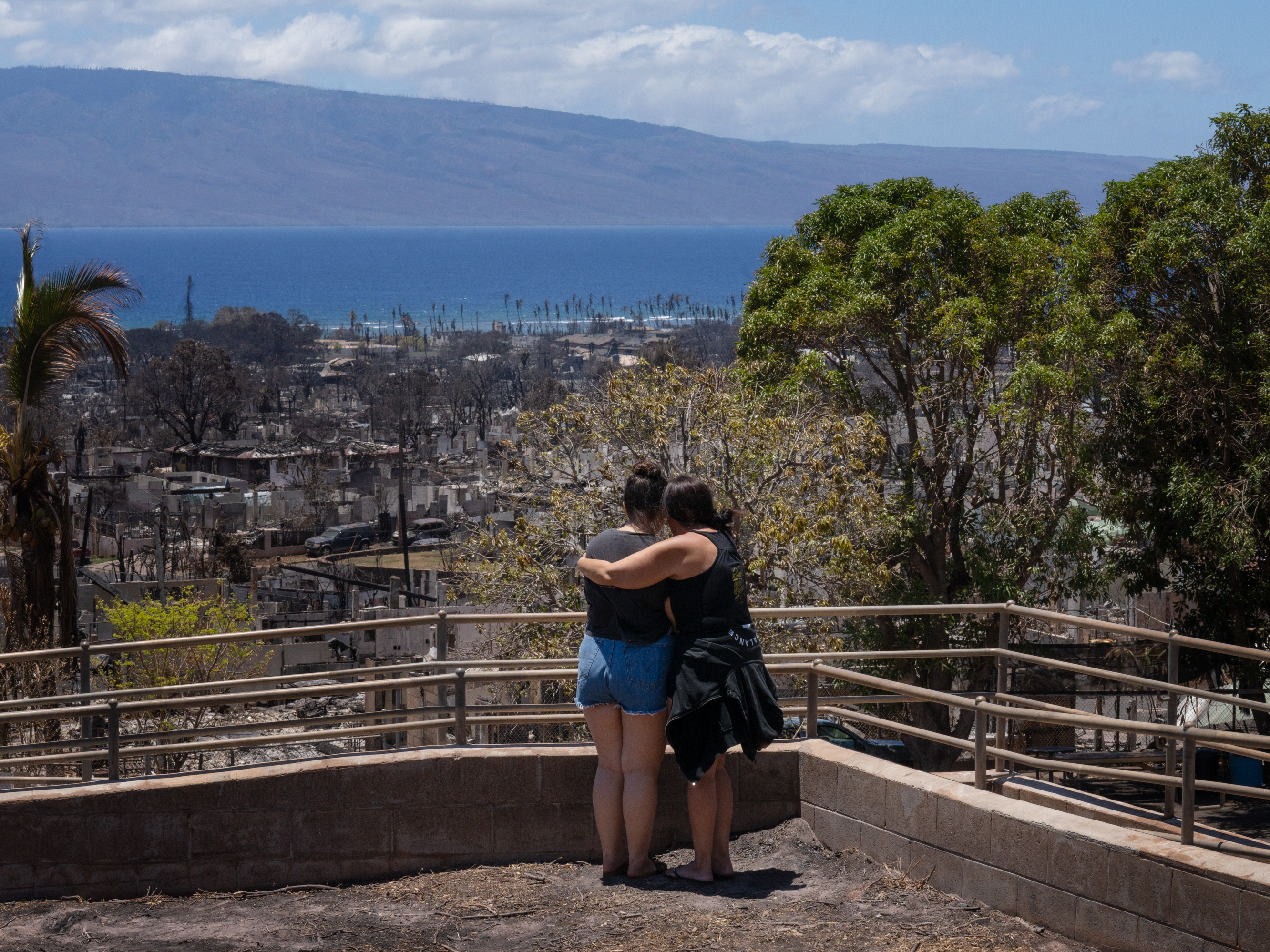 caption: Two women embrace and cry as they look out over Lahaina, in Maui, Hawaii, which was severely damaged by a wildfire in August.
