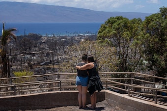 caption: Two women embrace and cry as they look out over Lahaina, in Maui, Hawaii, which was severely damaged by a wildfire in August.