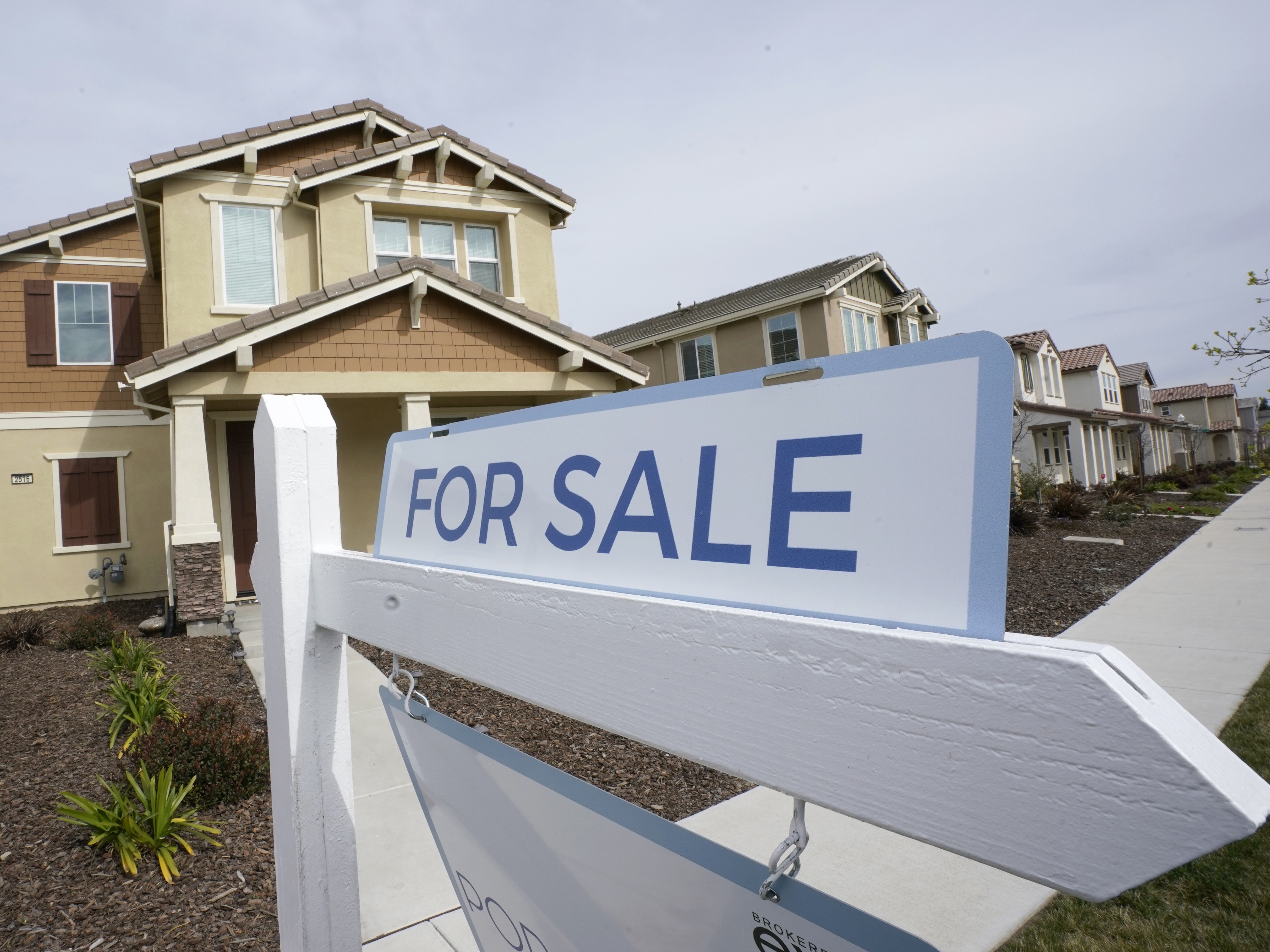caption: A for sale sign is posted in front of a home in Sacramento, Calif., in 2022.