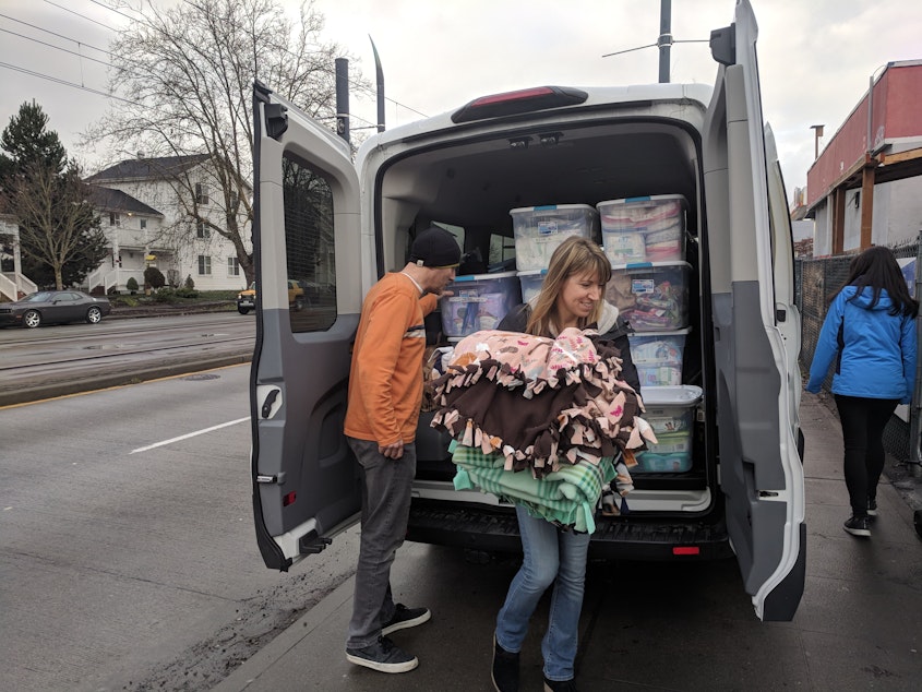 caption: Angela Harmon and fellow volunteers unpack blankets, diapers and other essentials in front of a tiny house village in Seattle