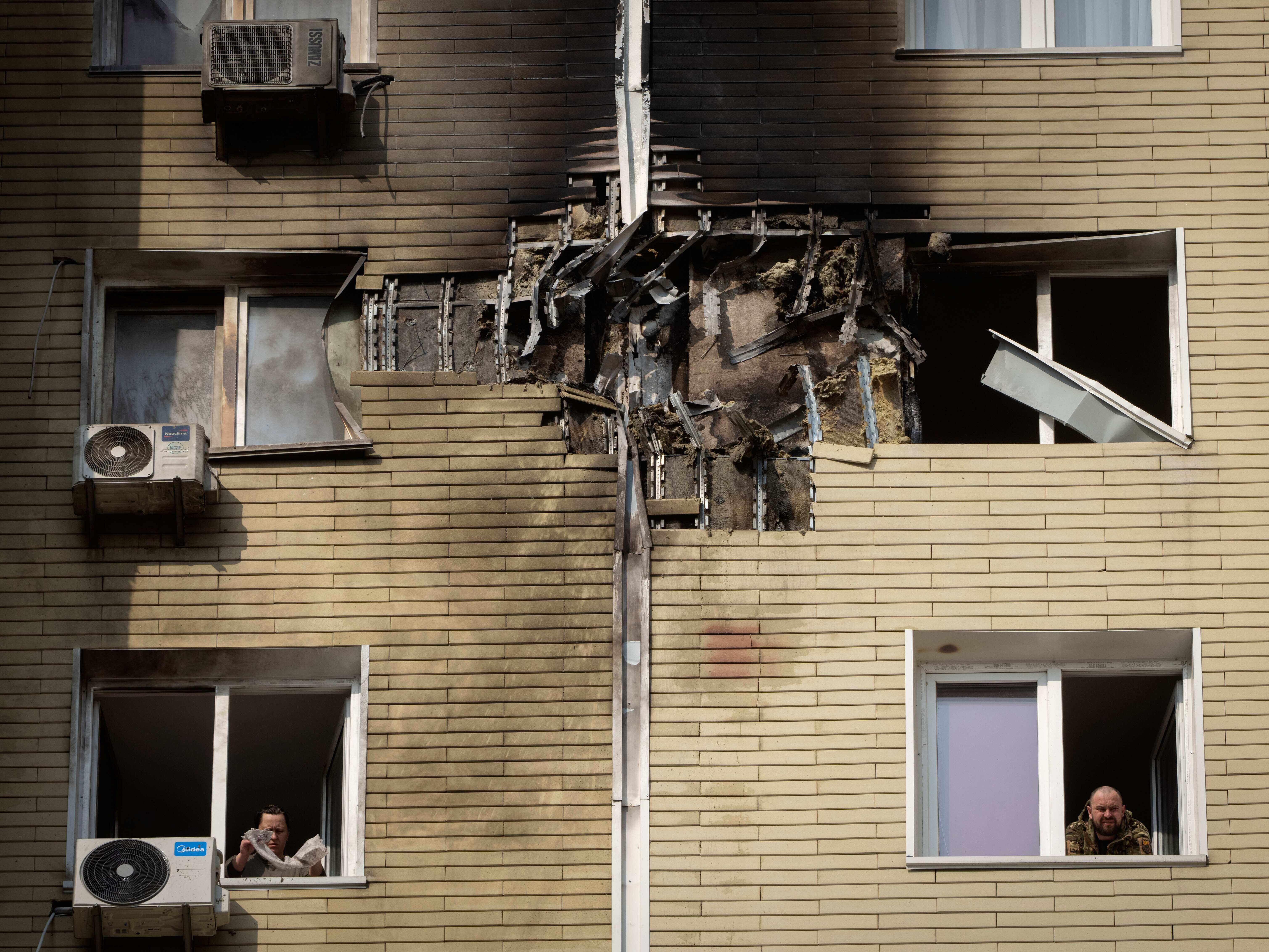 caption: A resident watches as his neighbor cleans up a damaged apartment after a Russian drone attack in Kyiv, Ukraine, March 23.