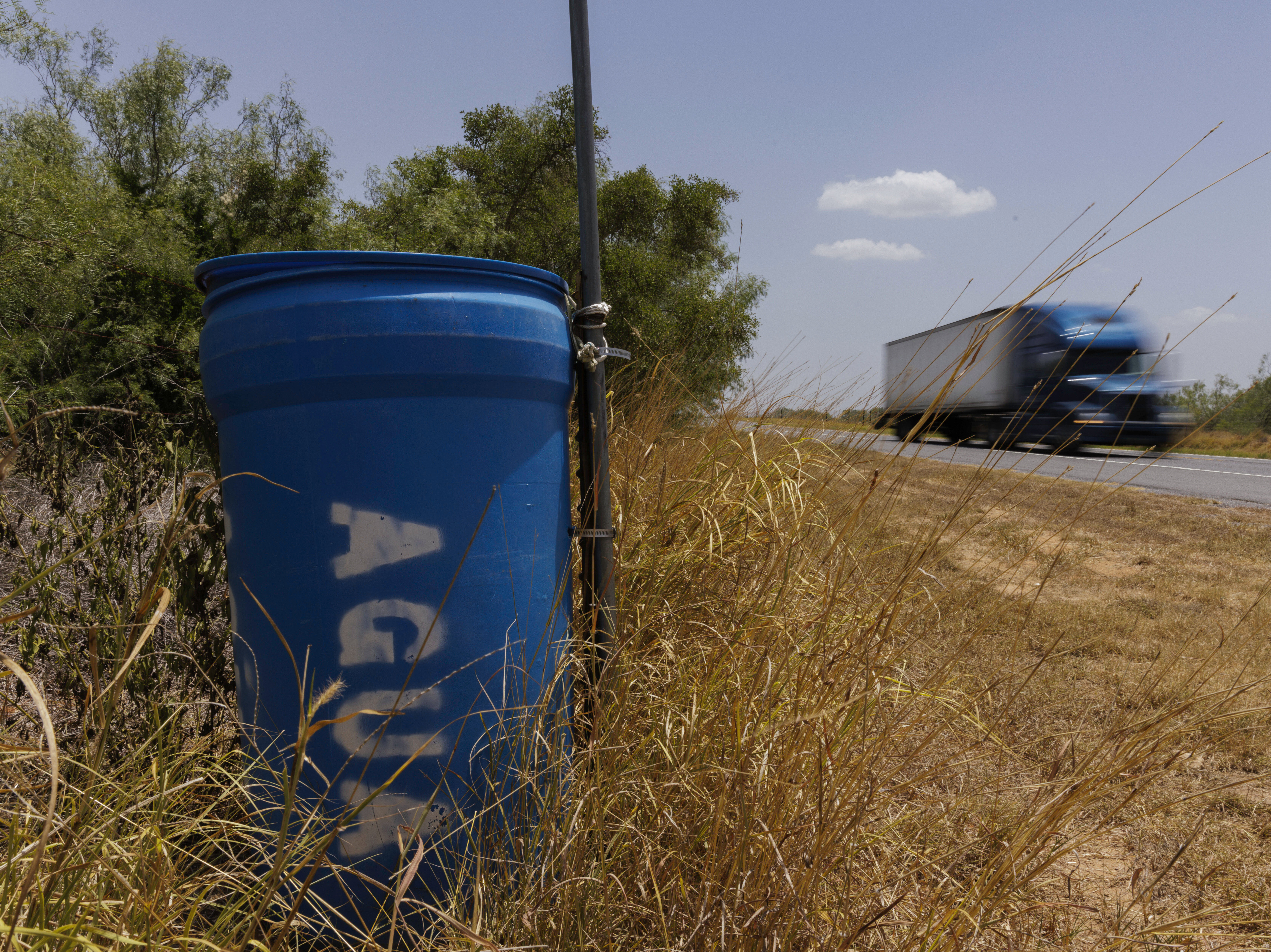 caption: A water station for immigrants containing sealed jugs of fresh water sits along a fence line near a roadway in rural Jim Hogg County, Texas, on July 25.