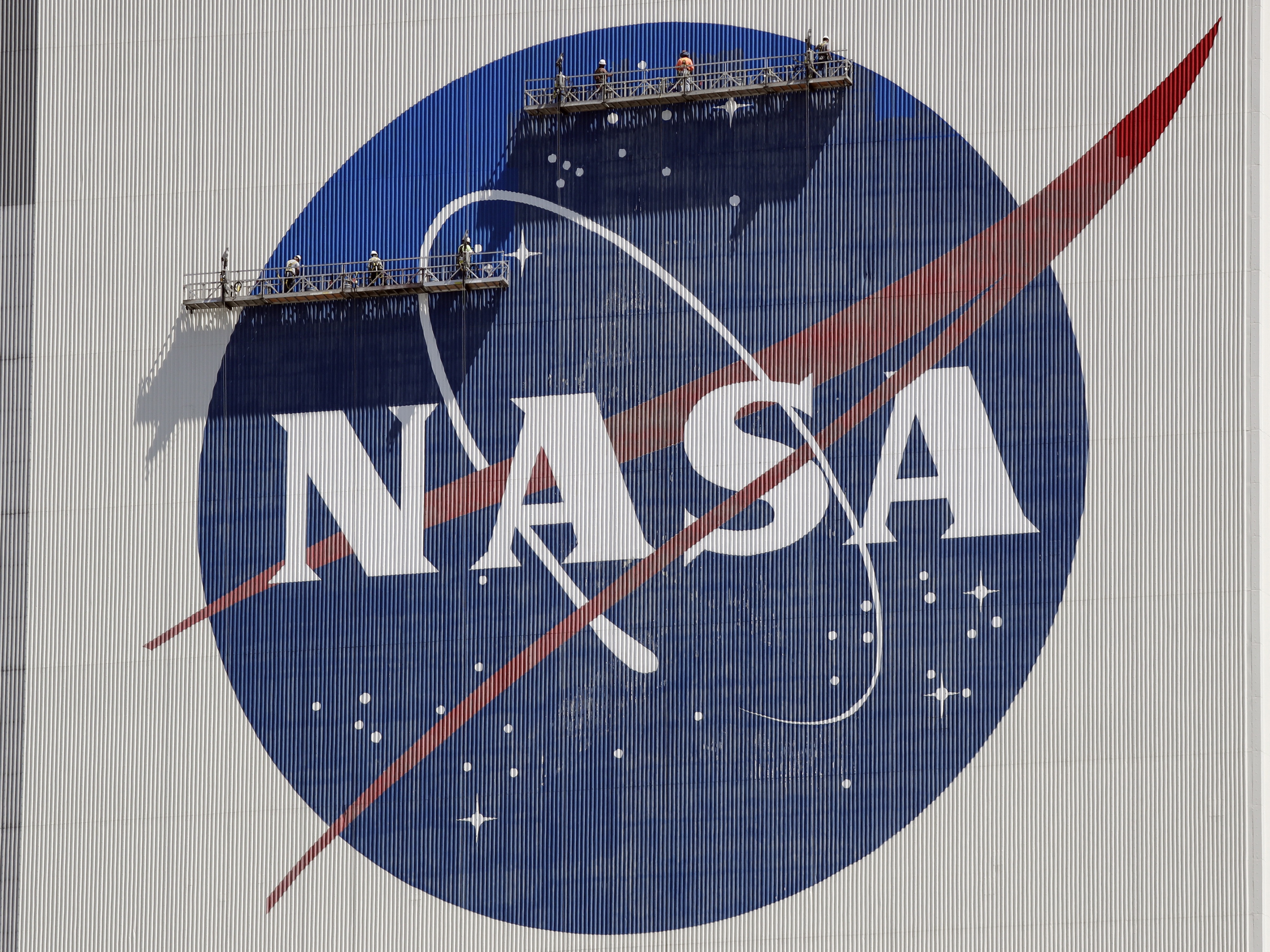 caption: Workers on scaffolding repaint the NASA logo near the top of the Vehicle Assembly Building at the Kennedy Space Center in Cape Canaveral, Fla., May 2020.