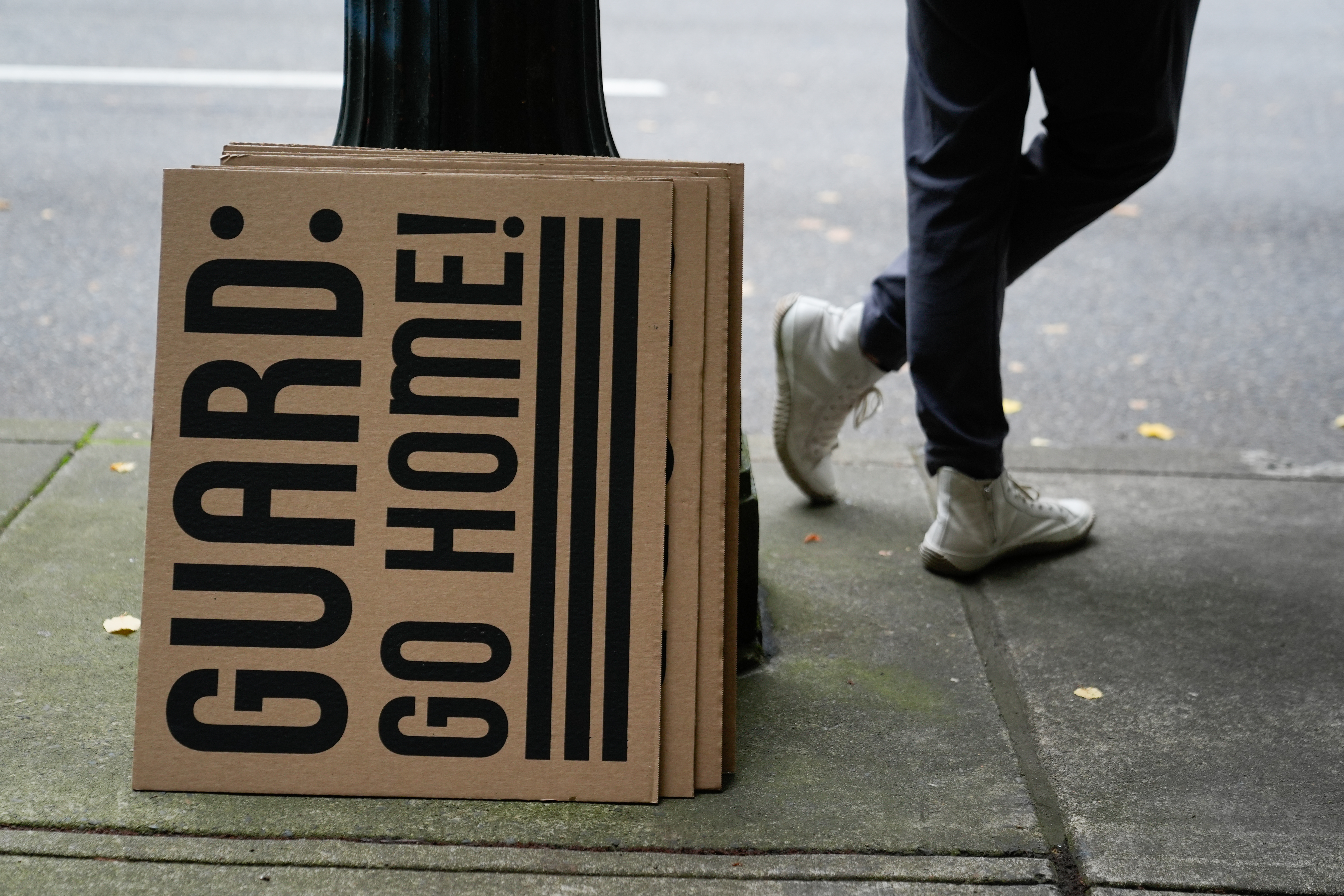 caption: A person stands by a sign that reads "Guard: Go Home!" while they protest outside the federal courthouse on Friday, Oct. 3, 2025, in Portland, Ore., as a federal court hearing on Oregon's bid to temporarily block President Donald Trump's deployment of the National Guard to Portland is held inside. 