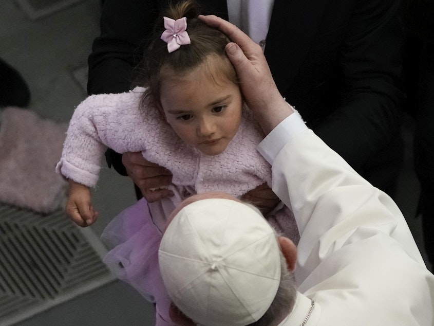 caption: Pope Francis caresses a child in the Paul VI hall at the Vatican, Friday, April 8, 2022. Italy's Constitutional Court ruled that children should receive both parents' surnames at birth, not just the father's.