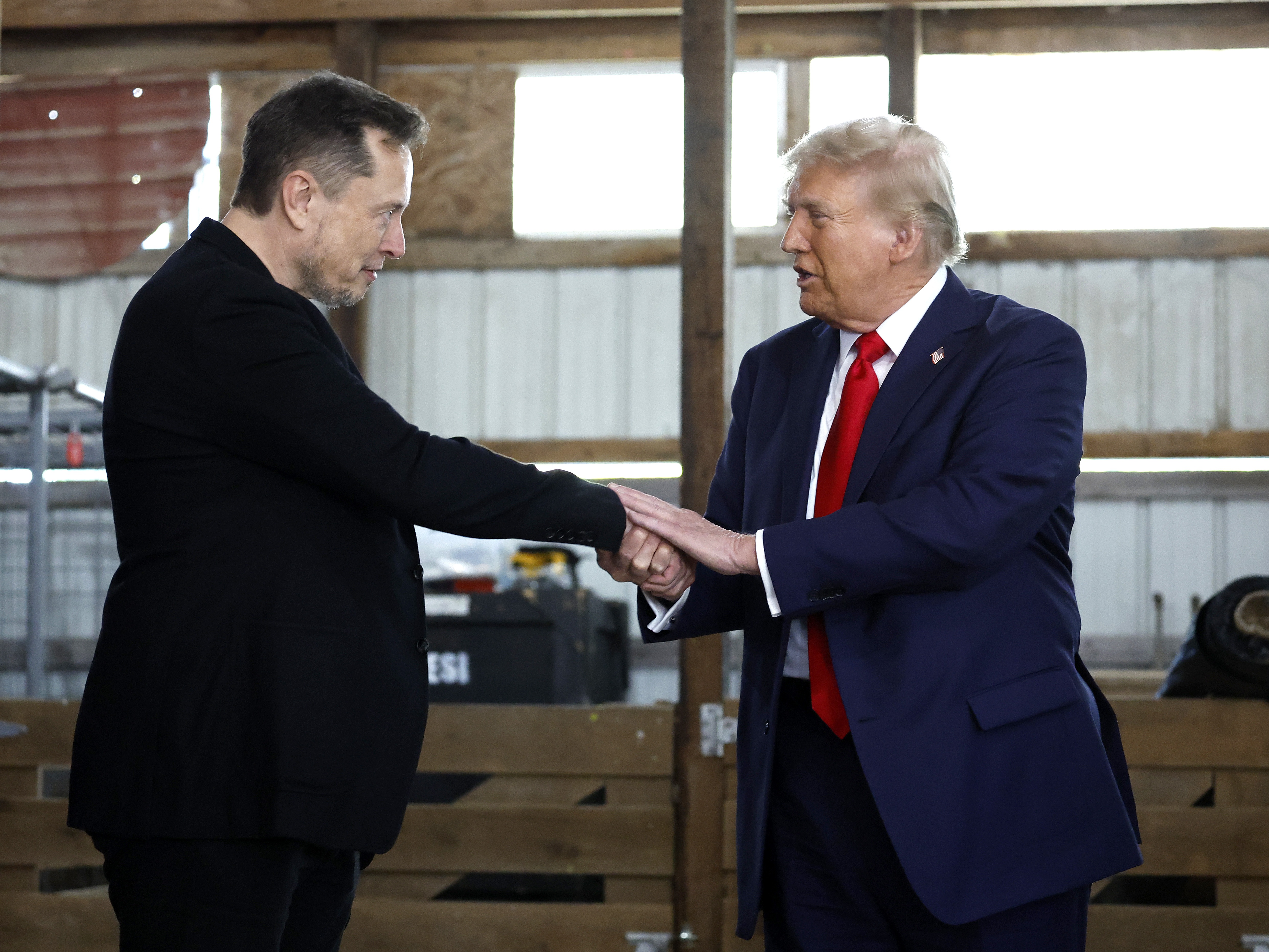 caption: President-elect Trump shakes hands with Elon Musk at a campaign stop in Butler, Pa., on October 5, 2024. Trump has named Musk and former presidential hopeful Vivek Ramaswamy co-leaders of a new commission called the "Department of Government Efficiency," which will advise and guide Trump in his quest to "dismantle government bureaucracy."