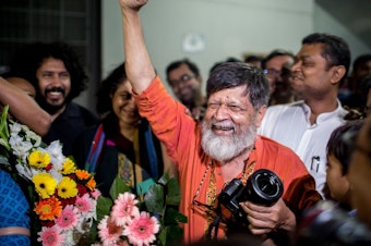 caption: Bangladeshi photographer and activist Shahidul Alam, center, reacts as he is released from Dhaka Central Jail, Keraniganj, near Dhaka on Tuesday.