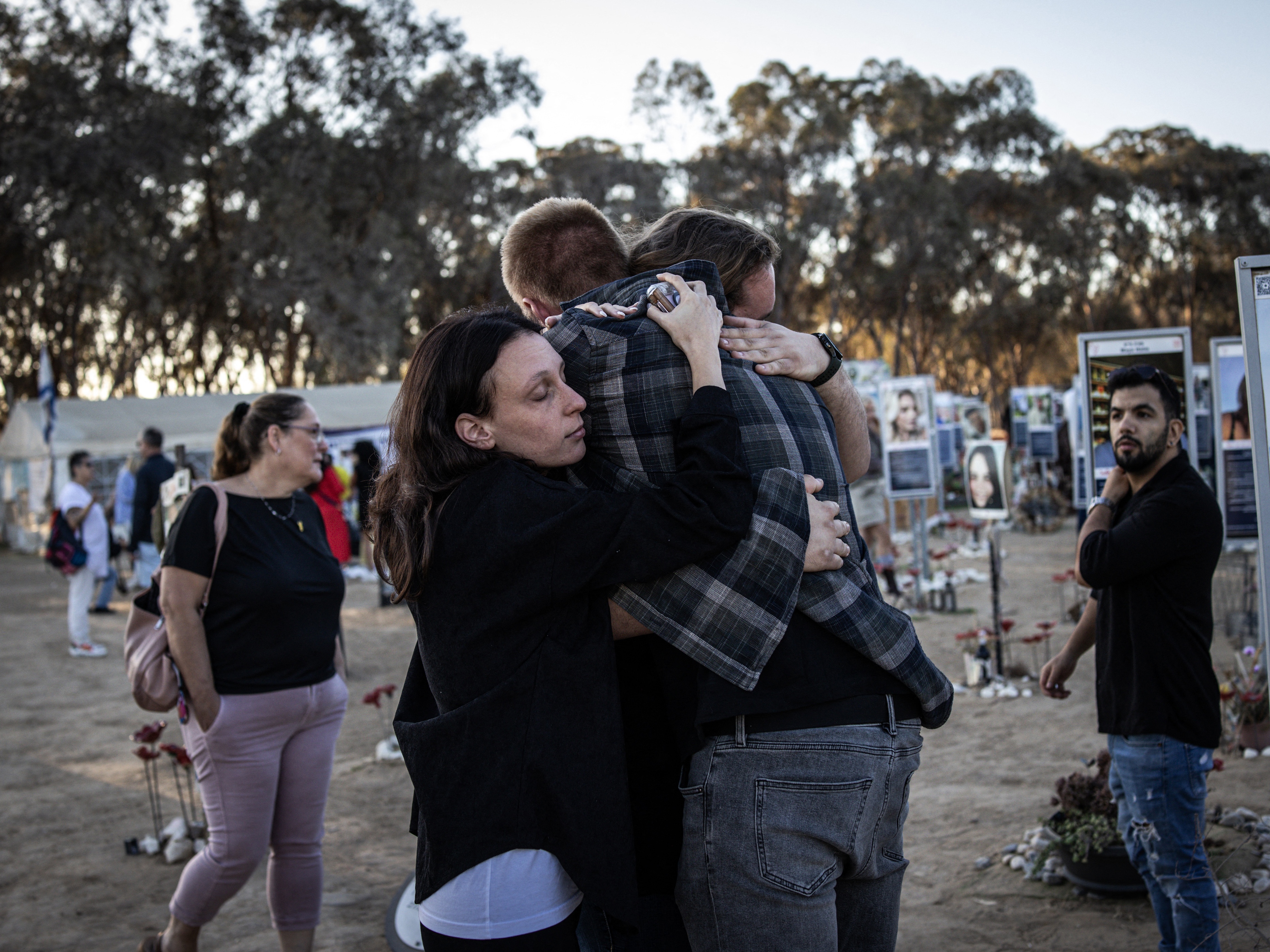 caption: People embrace next to memorials of victims of the Oct. 7, 2023, attacks at the Nova Festival grounds in Reim, in southern Israel, on the second anniversary of the Hamas-led attacks on Tuesday.