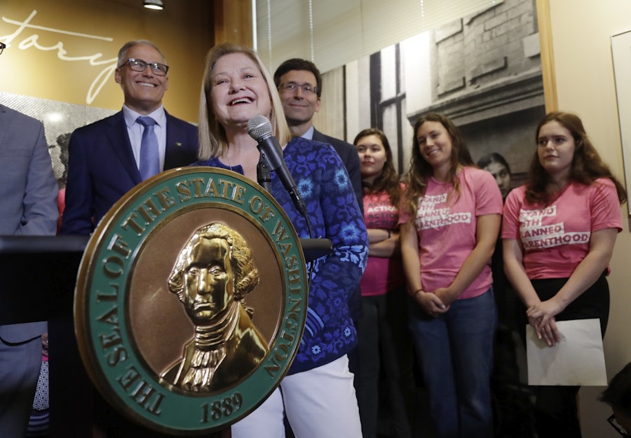 caption: Planned Parenthood of the Great Northwest and the Hawaiian Islands CEO Chris Charbonneau speaks at a news conference addressing a change in rules on the nearly 50-year-old Title X family planning program as Gov. Jay Inslee, left, and Washington Attorney General Bob Ferguson look on, Thursday, Aug. 22, 2019, in Seattle. King County Executive Dow Constantine, second left, , right, and Washington Attorney General Bob Ferguson, third right, look on. 