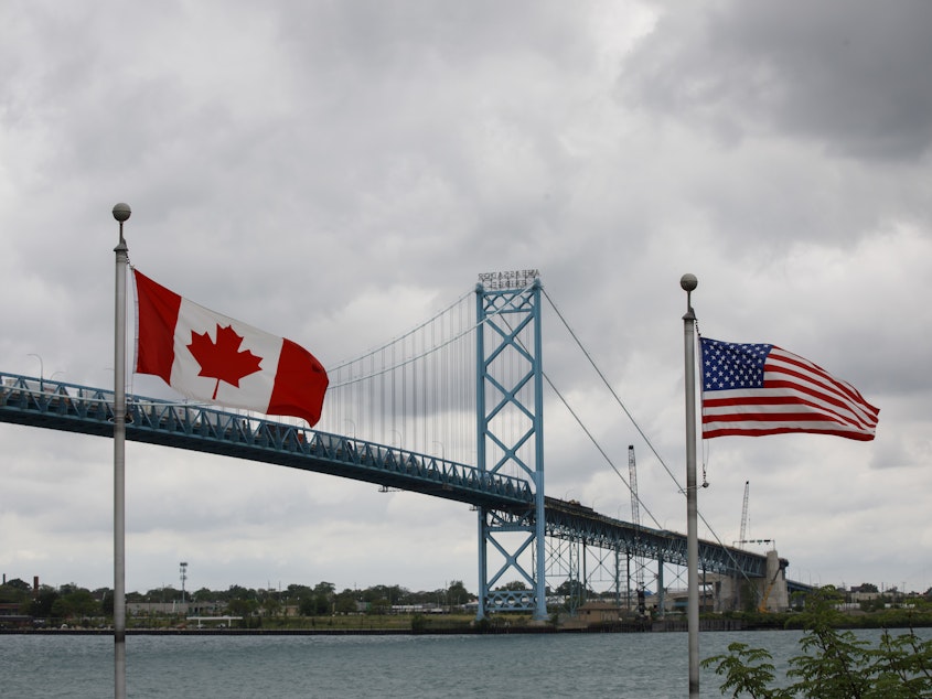 caption: Canadian and American flags fly near the Ambassador Bridge connecting Canada to the U.S. in Windsor, Ontario, in May. Half of respondents in a poll of Canadians this month by Nanos Research said restrictions on travel across the U.S.-Canada border should not be eliminated until this fall or next year.