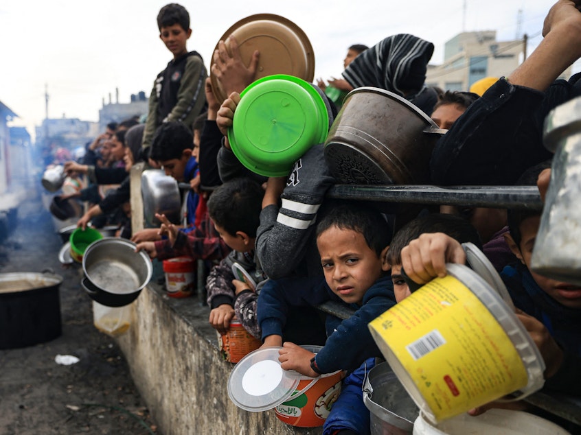 caption: Palestinian children wait to collect food at a donation point in a refugee camp in Rafah in the southern Gaza Strip on December 23, 2023.