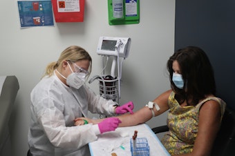 caption: Leyda Valentine, a research coordinator, takes blood from Lisa Taylor as she participates in a COVID-19 vaccination study at Research Centers of America in Hollywood, Fla., in August 2020.