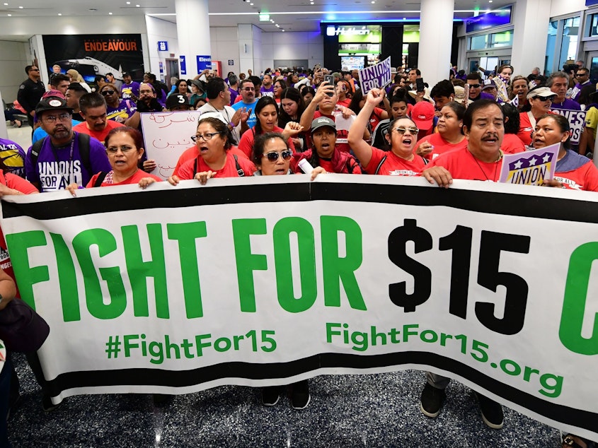 caption: Airport employees, Uber and Lyft drivers, and other workers protest for a $15 minimum wage at Los Angeles International Airport in October. Increases in minimum wages contributed to bigger pay gains for lower-income workers.